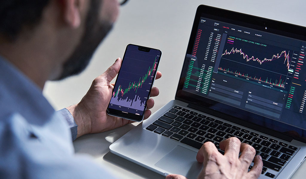 رجل يستخدم جهاز الكمبيوتر المحمول الخاص به وهاتفه لتحليل البيانات